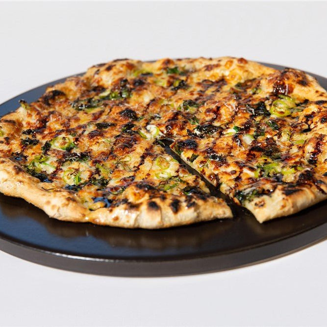 Grilled pizza with charred crust, white sauce and banana peppers on a black plate