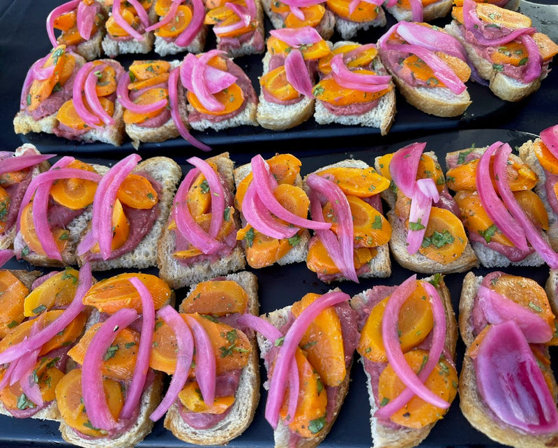 Plated appetizers with pink pickled onions and orange slices on a black plate