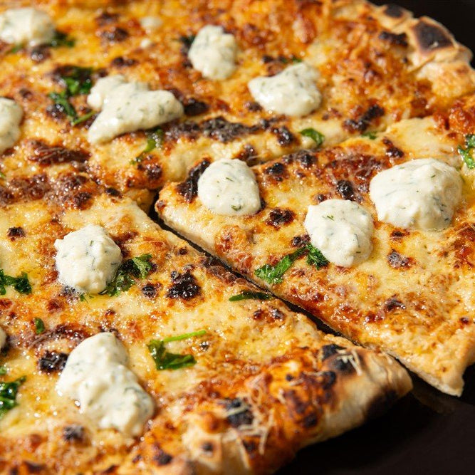 Close-up of a grilled pizza with cheeses and herbs on a black plate