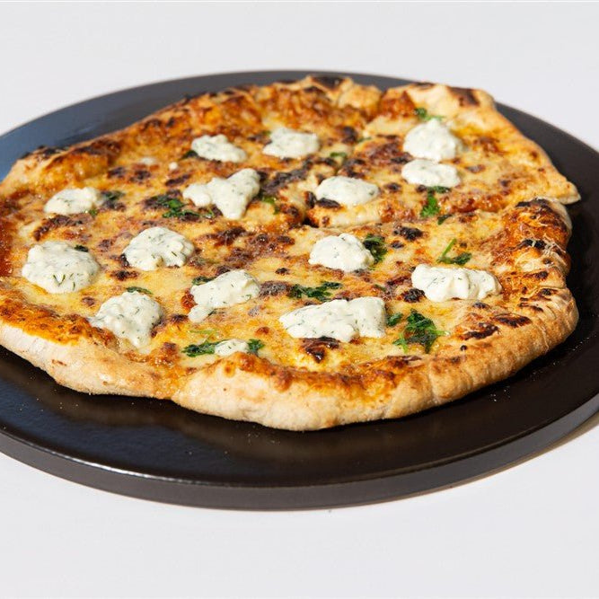 Close-up of a grilled pizza with cheeses and herbs on a black plate