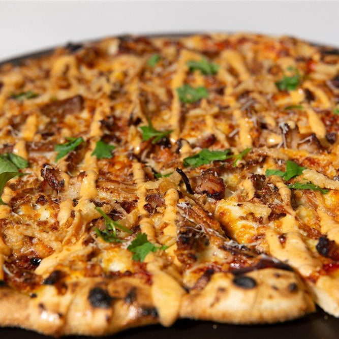 Personal-sized grilled pizza with bourbon bbq pork on a black plate
