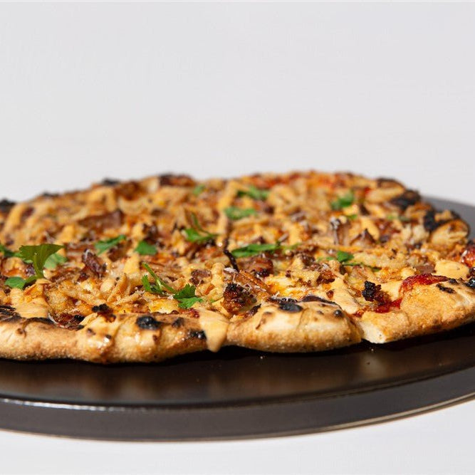 Personal-sized grilled pizza with bourbon bbq pork on a black plate