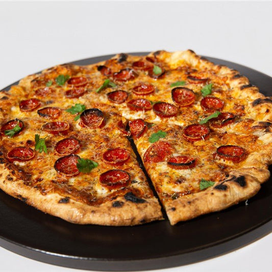 Pizza with pepperoni and green toppings on a black pan