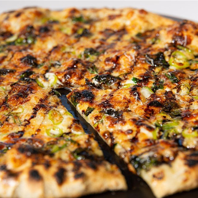 Grilled pizza with charred crust, white sauce and banana peppers on a black plate