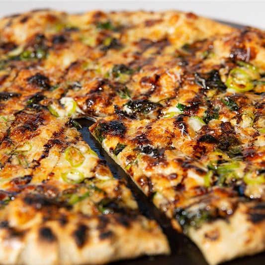 Grilled pizza with charred crust, white sauce and banana peppers on a black plate